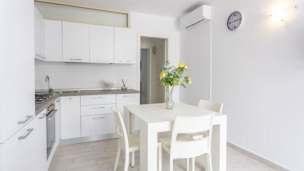 A modern kitchen with white cabinetry, a dining table with chairs, and a vase with flowers. - Condoluci Apartment - Tropea (Tropea)
