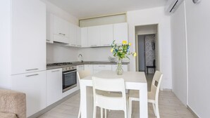 A modern kitchen with white cabinetry, a dining table with four chairs, and a vase with flowers on the table. - Condoluci Apartment - Tropea (Tropea)