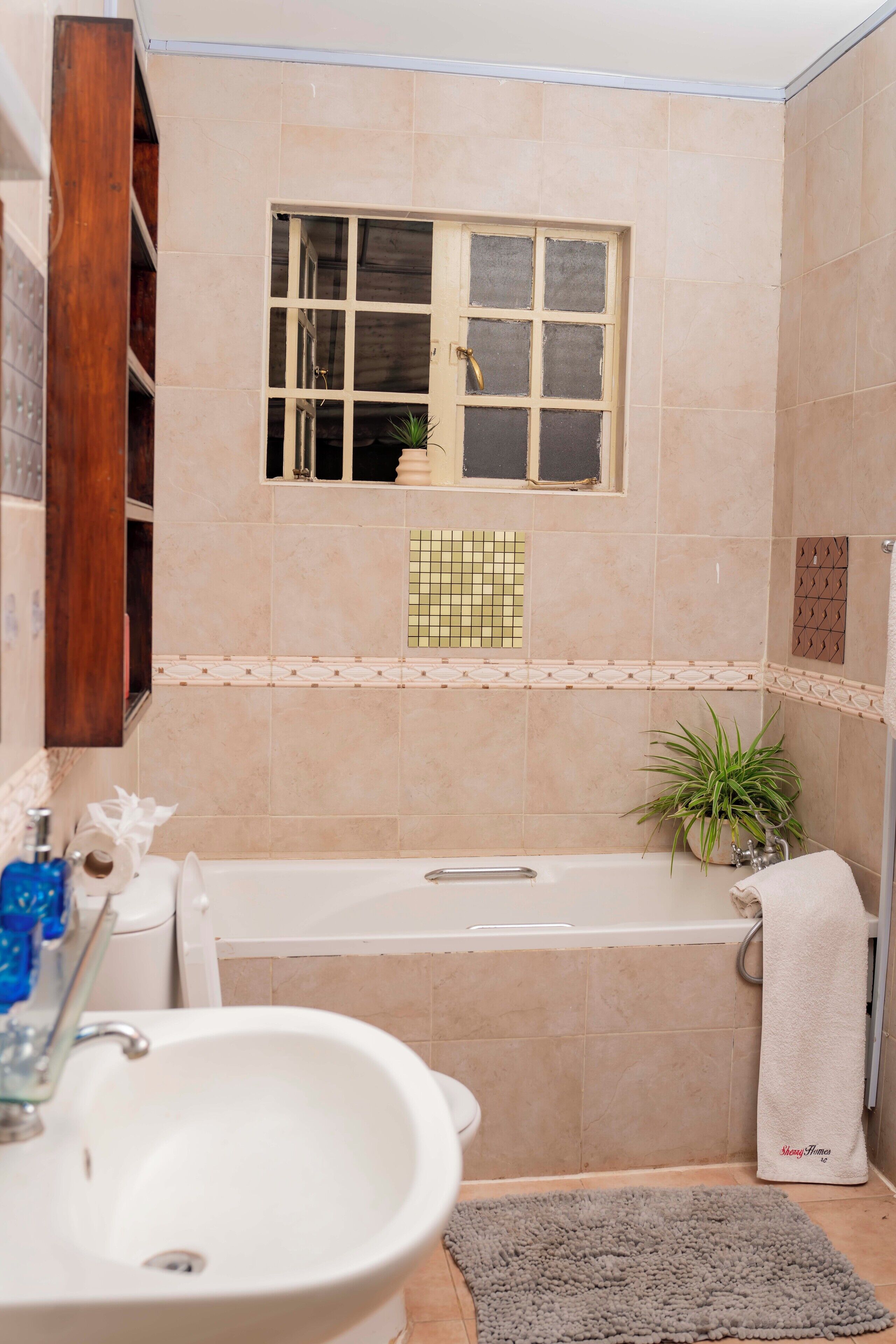 A bathroom with a bathtub, a sink, a window, and a potted plant.