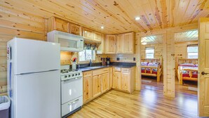 A wooden cabin interior with a kitchen area, including a refrigerator, stove, microwave, and wooden cabinets. - Lakefront Cabin w/ Dock, Fire Pits in Danbury! (Danbury)