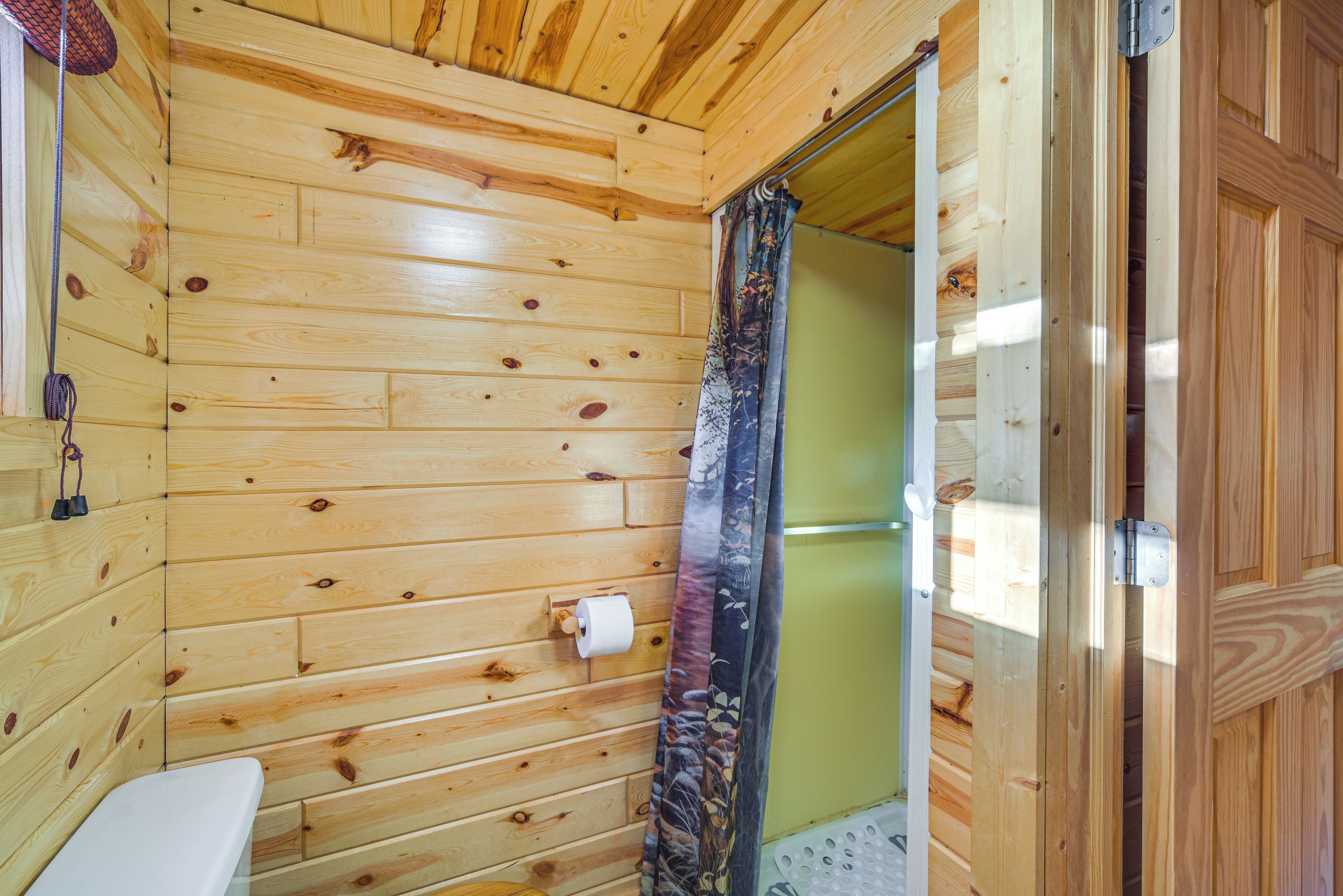Baño de cabaña de madera con inodoro, cortina de ducha y puerta de madera.