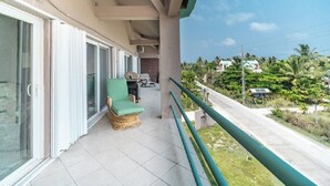 A balcony with a wicker chair, a small table, and a view of a road and greenery. - Mara Laguna Condo San Pedro Belize (San Pedro)