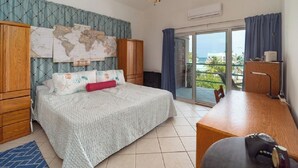 A bedroom with a bed, a desk, a ceiling fan, a world map on the wall, and a view of the outdoors through a glass door. - Mara Laguna Condo San Pedro Belize (San Pedro)