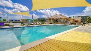 A swimming pool with a wooden deck, lounge chairs, and a thatched-roof structure. - Mara Laguna Condo San Pedro Belize (San Pedro)