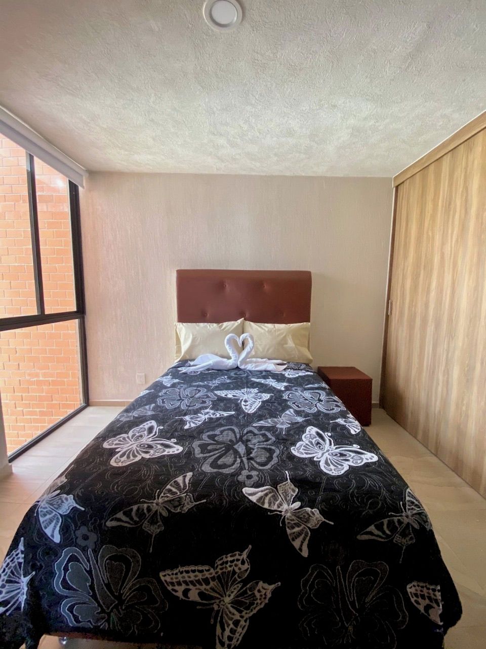 Een slaapkamer met een bed, nachtkastje, raam en deur.