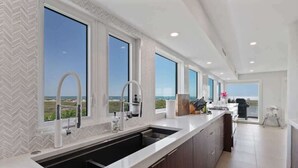 A modern kitchen with large windows, a built-in sink, and a view of the ocean. - Shangri-La | Bean Point | Rooftop Pool | Golf Cart (Anna Maria)