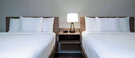 A hotel room with two beds, a nightstand with a lamp, and a wooden floor.