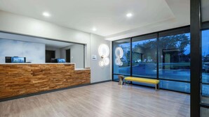 A reception area with a wooden reception desk, a bench, and large windows with a view of the outside. - ECHO Suites Extended Stay by Wyndham Spartanburg (Spartanburg)