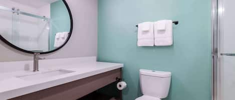 A modern bathroom with a white sink, a round mirror, a toilet, and a glass shower enclosure.