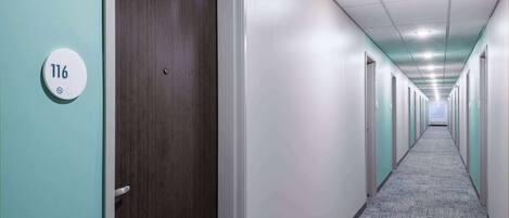 A hallway with a carpeted floor, doors on both sides, and a sign indicating room number 116.