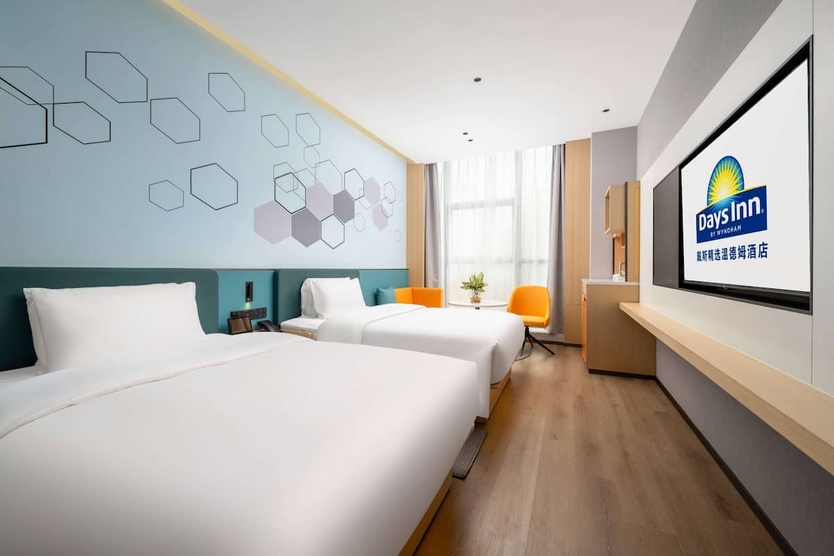 Habitación de hotel con dos camas, televisión, escritorio y ventana con cortinas.
