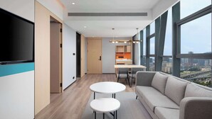 Une chambre d’hôtel moderne dotée d’une grande télévision, d’un canapé, d’un coin repas et offrant une vue sur la ville.