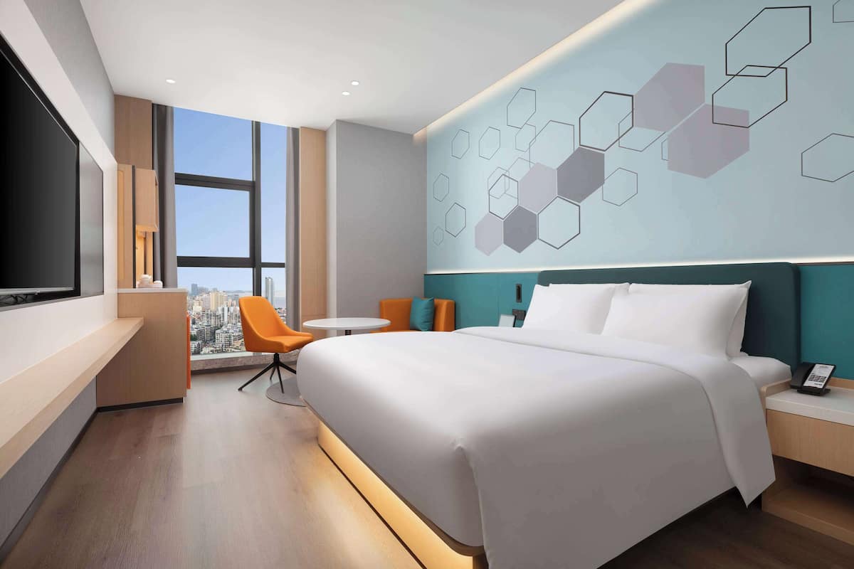 Una habitación de hotel moderna con una cama grande, un escritorio, una silla y un televisor.