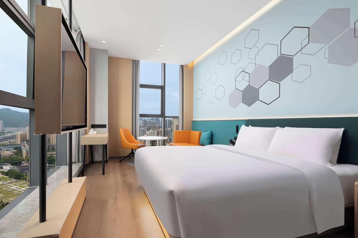Una habitación de hotel moderna con una cama grande, un escritorio y una silla, vistas a la ciudad y un diseño geométrico en la pared.