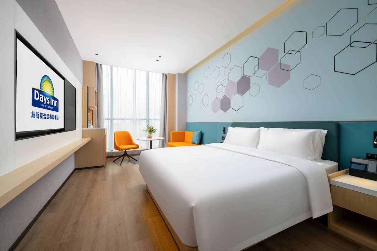 Habitación de hotel con una cama grande, un escritorio, una silla y un televisor mostrando el logotipo de Days Inn.