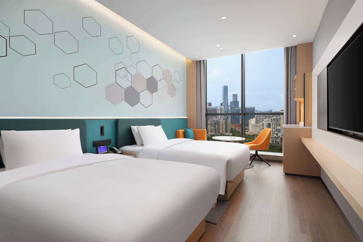 Habitación de hotel con dos camas, un escritorio, televisión y vista a la ciudad.