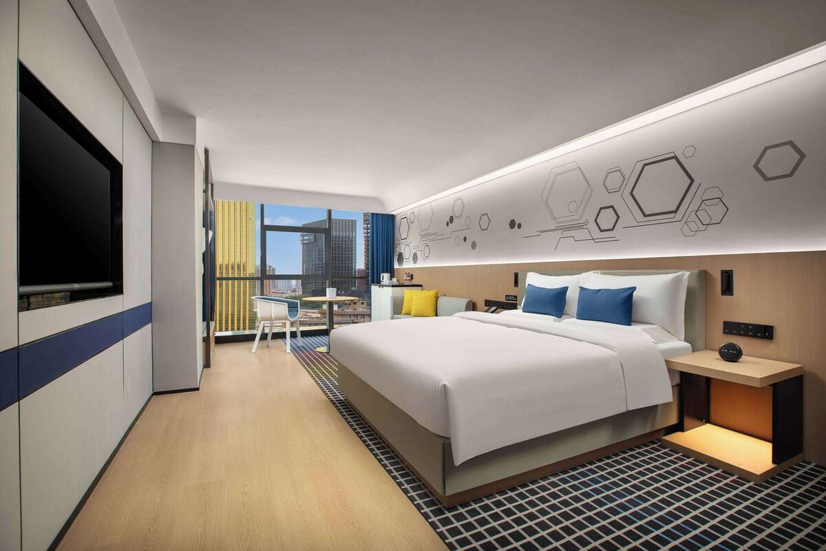 Una habitación de hotel moderna con una cama grande, mesita de noche y vistas a la ciudad.