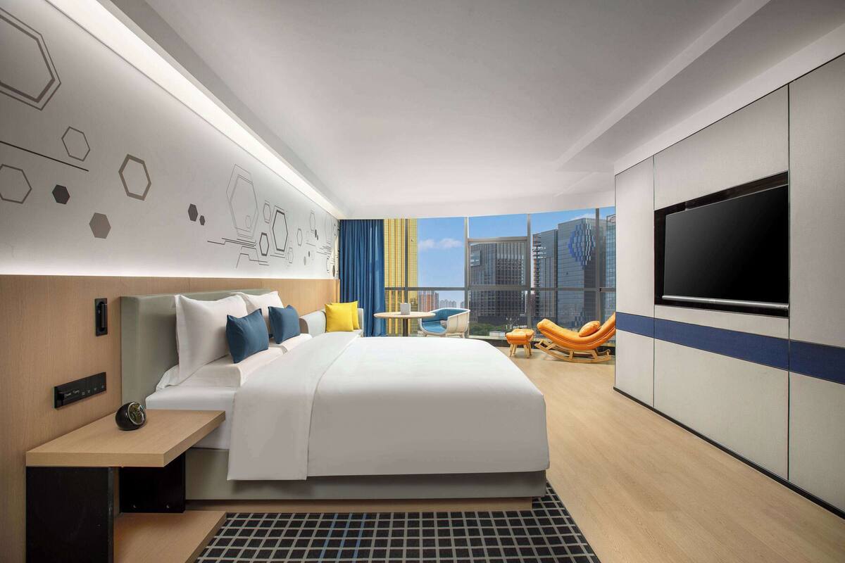 Habitación de hotel moderna con una cama grande, un escritorio, un televisor de pantalla plana y vistas a la ciudad.