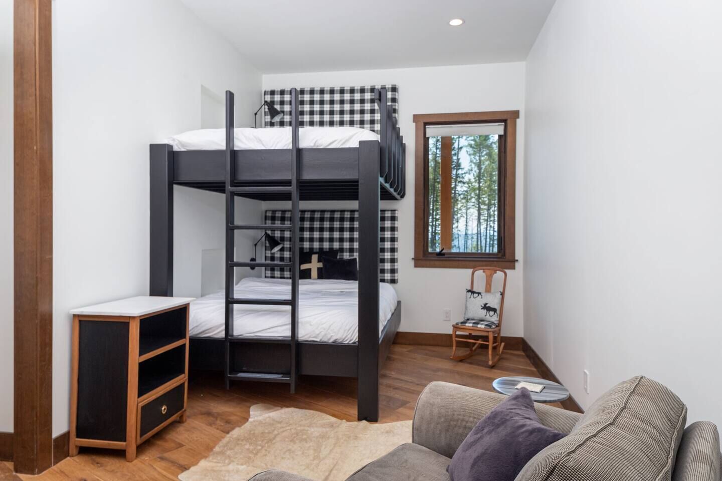 Une petite pièce comprenant un lit superposé, une petite armoire en bois, un fauteuil à bascule et une fenêtre donnant sur des arbres.