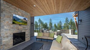 A modern outdoor living area with a stone fireplace, a sofa, and a coffee table. - Great Northern Mountain Escape (Whitefish)