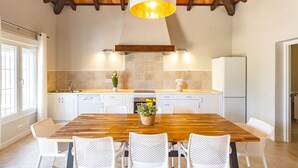 A kitchen with a wooden table, white chairs, a hanging light fixture, and a refrigerator. - Cubo's La Luz del Valle Rural House / air conditioning / free wifi / BBQ / private pool (Alhaurín el Grande)