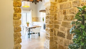 A stone-walled corridor leading to a dining area with a wooden table and chairs, a hanging light fixture, and a potted plant. - Cubo's La Luz del Valle Rural House / air conditioning / free wifi / BBQ / private pool (Alhaurín el Grande)
