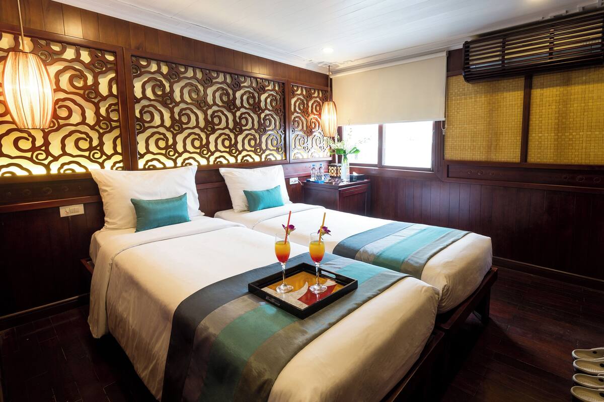 A hotel room with two beds, a decorative headboard, a tray with drinks, and a window with a view.