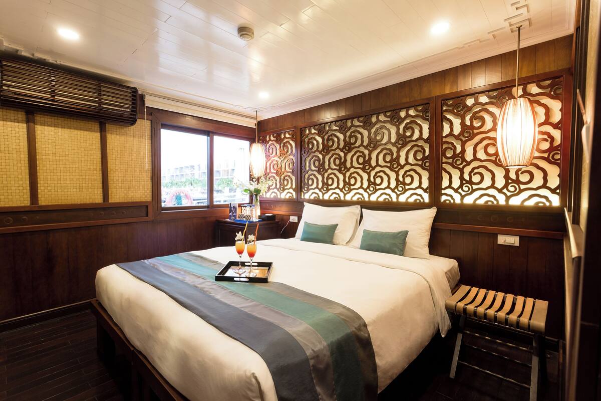 A hotel room with a large bed, a bedside table with a tray of drinks, a bench, and a decorative wall panel.