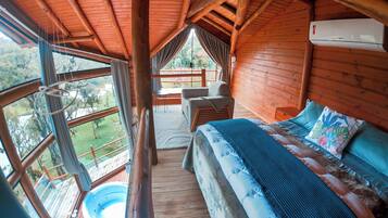 Una cabaña de madera con una cama grande, un jacuzzi y un balcón con vistas al exterior.