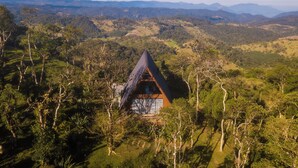 A remote, triangular-roofed cabin surrounded by dense forest, with a panoramic view of distant mountains. - Casa da Mata (Sao Bento do Sul)