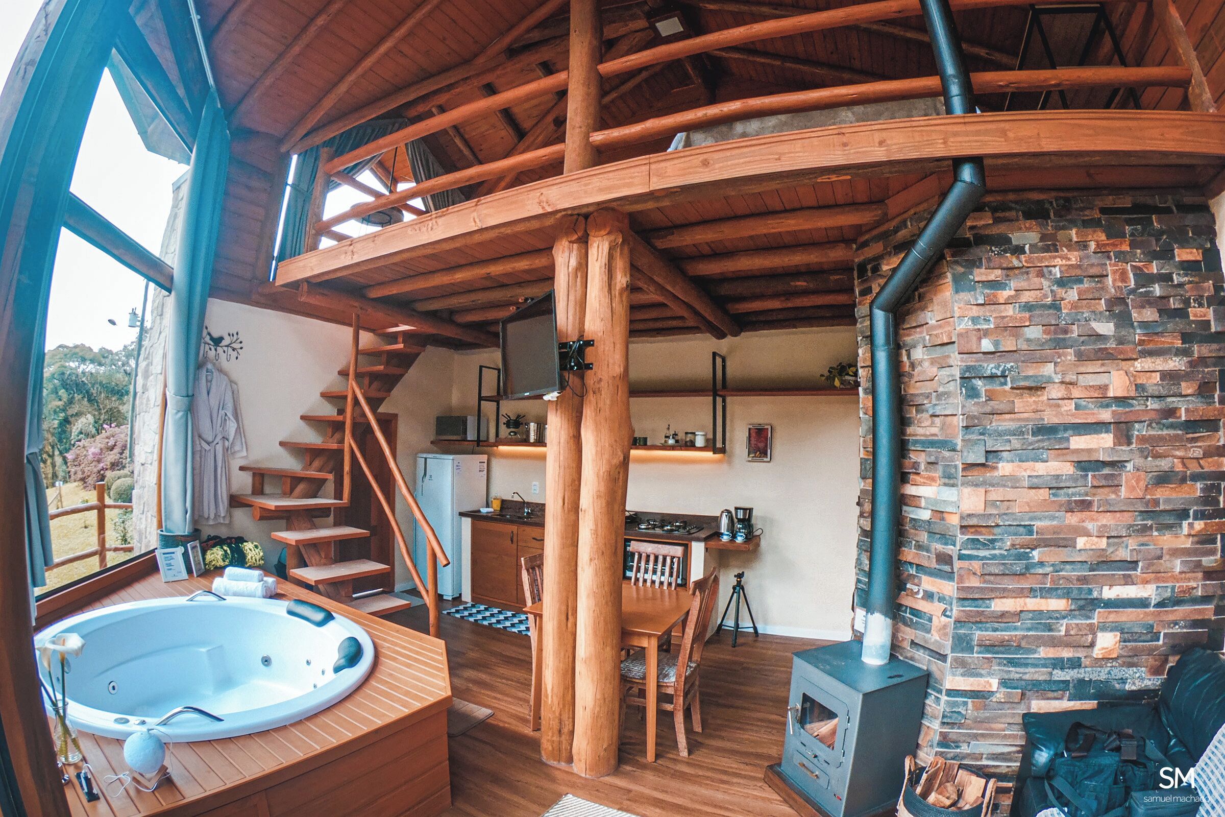 Un interior de madera con un jacuzzi, una chimenea y una escalera que sube a una buhardilla.