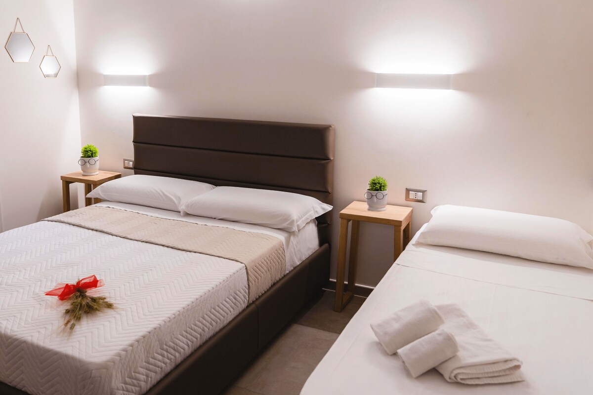 A modern hotel room with a large bed, bedside tables, and wall-mounted lighting.