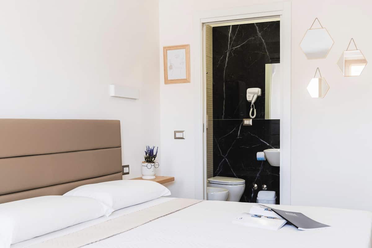 A modern hotel room with a bed, bedside table, and a bathroom visible through an open door.
