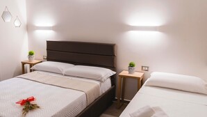 A neatly made bed with a white comforter and a red bow, a bedside table with a small plant, and a wall-mounted light fixture.