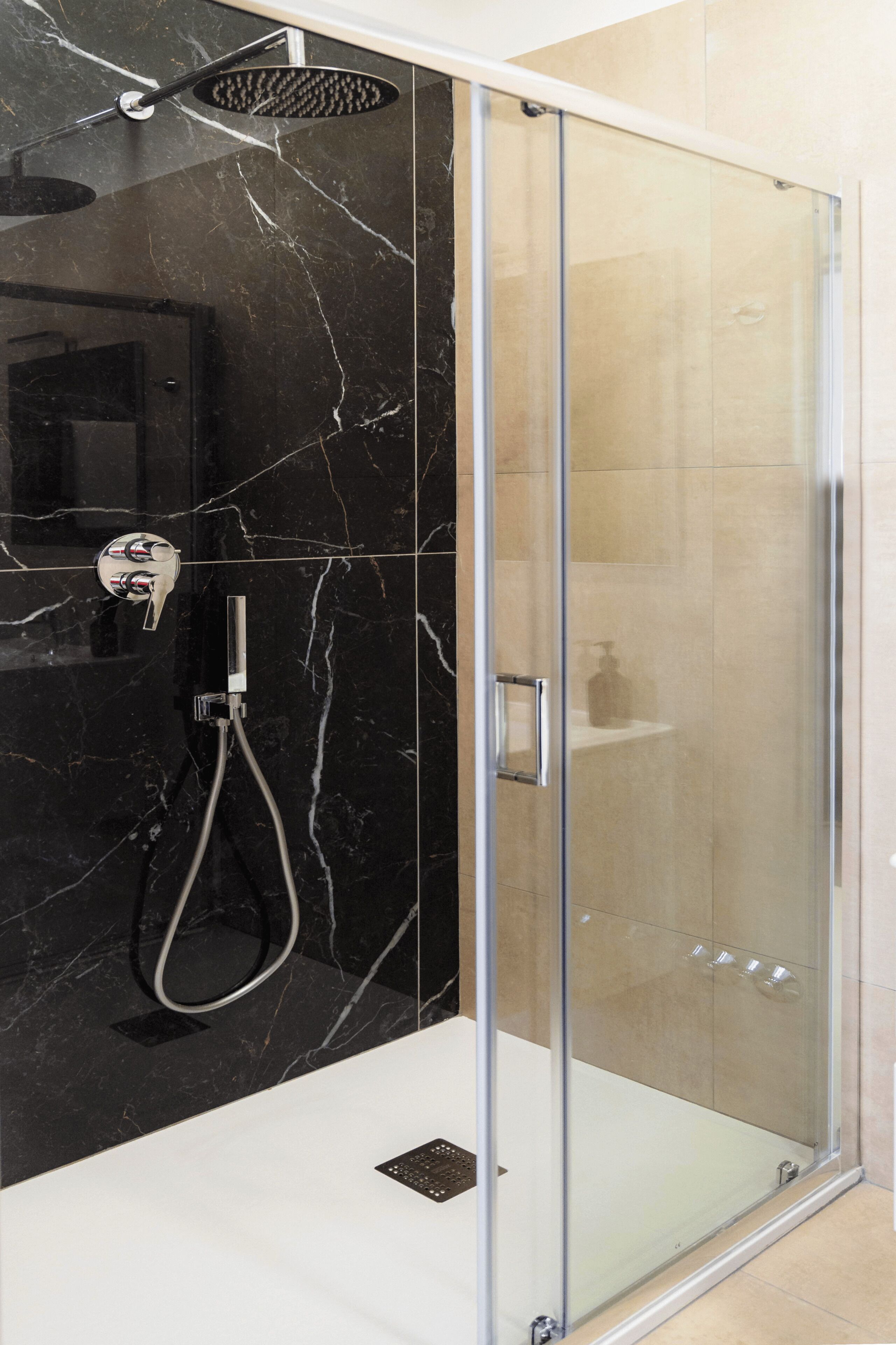 Een moderne badkamer met een glazen douchecabine, een handdouche en een wandmengkraan.