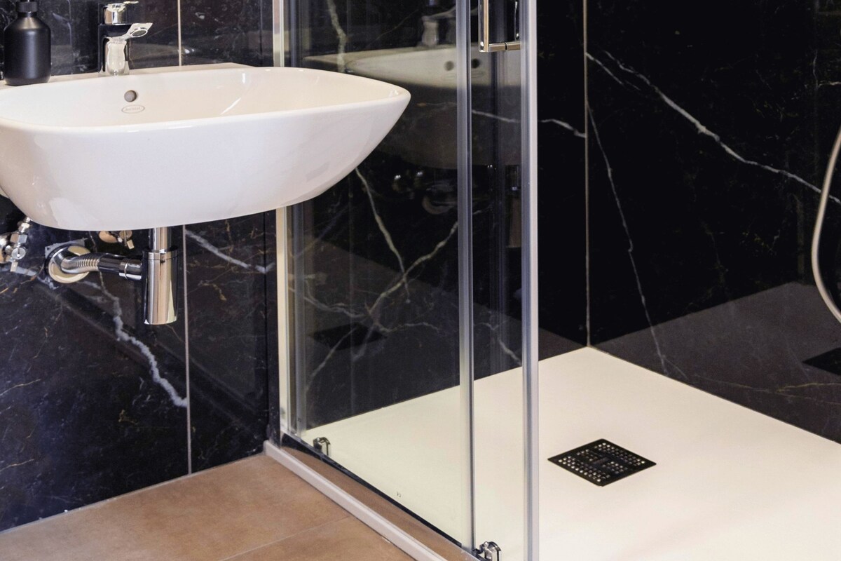A modern bathroom with a glass-enclosed shower, a white sink, and a marble-tiled wall.