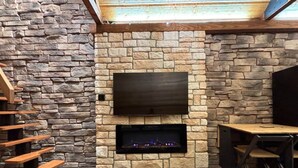 Una chimenea de piedra con un televisor de pantalla plana encima, bancos de madera y un adorno rústico.
