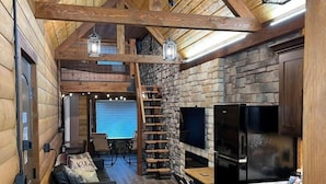Un interior de cabaña acogedor con chimenea de piedra, vigas de madera y una zona de cocina.