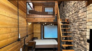 Una habitación compacta con cama alta, escritorio y escalera frente a una pared de piedra.