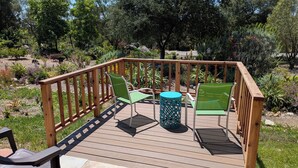 Une terrasse en bois avec une table et des chaises, entourée d’un jardin où poussent différentes plantes et arbres.