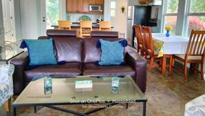 Un salon moderne avec un canapé en cuir marron, une table basse en verre et un coin repas comprenant des chaises et une table en bois.