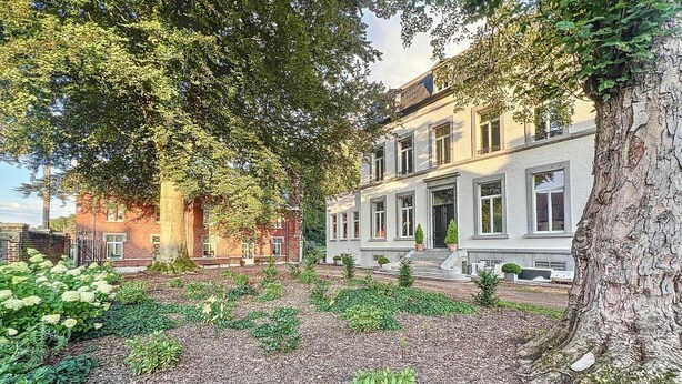 A large, two-story building with a symmetrical facade, a central entrance with steps, and a well-maintained garden with mulch and various plants. - Chateau La Fontaine - stylish accomodation - green environment (Mons)