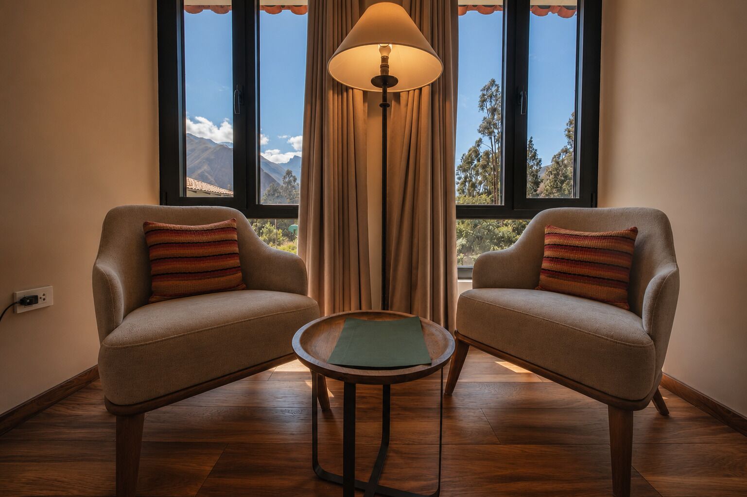 A room with two sofas, a small round table, a lamp, and a view of mountains through large windows.