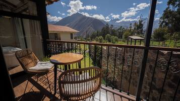 Varanda com cadeiras de vime e uma mesa, com vista para uma paisagem montanhosa.