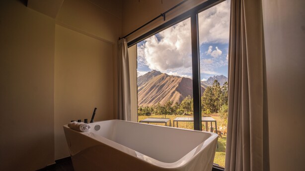 Un baño con bañera, una ventana con cortinas y vistas a montañas.