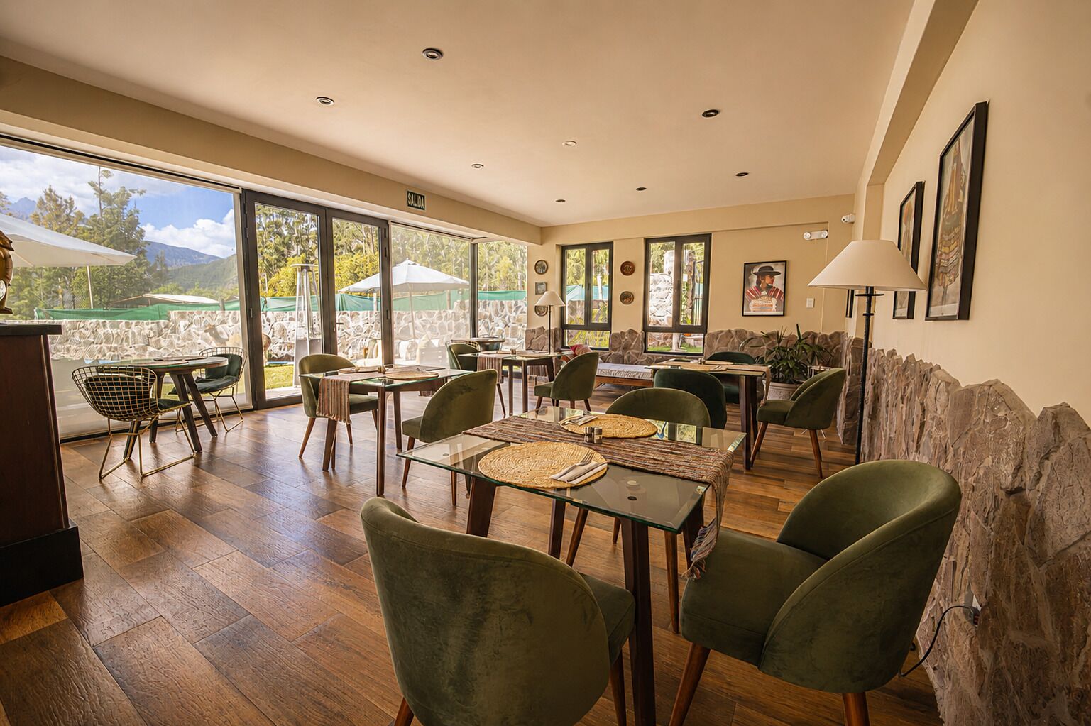 A dining area with tables and chairs, a stone wall, and a view of the outdoors.