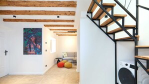 A modern interior with exposed wooden beams, a staircase with wooden steps and black metal railings, a washing machine, and a colorful abstract painting on the wall. - Black Water Bay house (Dubrovnik)