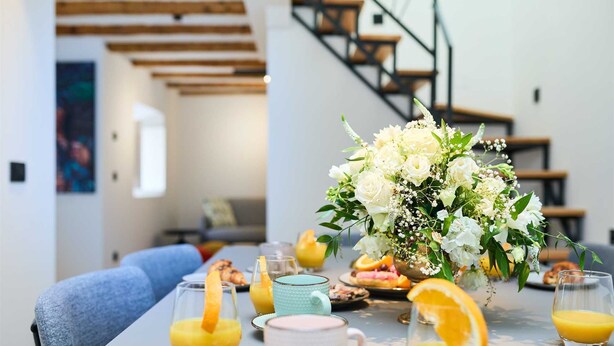 A breakfast setting with a table set for two, featuring orange juice, pastries, and a floral centerpiece. - Black Water Bay house (Dubrovnik)