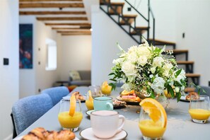 Ein Frühstückstisch für zwei Personen, mit Orangensaft, Gebäck und einem Blumenarrangement.