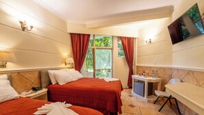 Habitación de hotel con dos camas, un escritorio pequeño, un televisor y una ventana con cortinas.